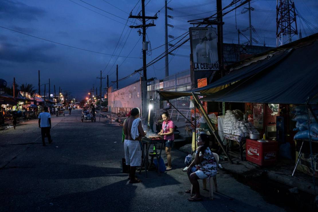 Pracownicy portu i rybacy kupują jedzenie od ulicznego sprzedawcy w porcie Navotas w Manili