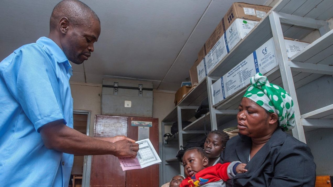 Sanitariusz wydaje kobiecie medyczny paszport do monitorowania programu szczepień